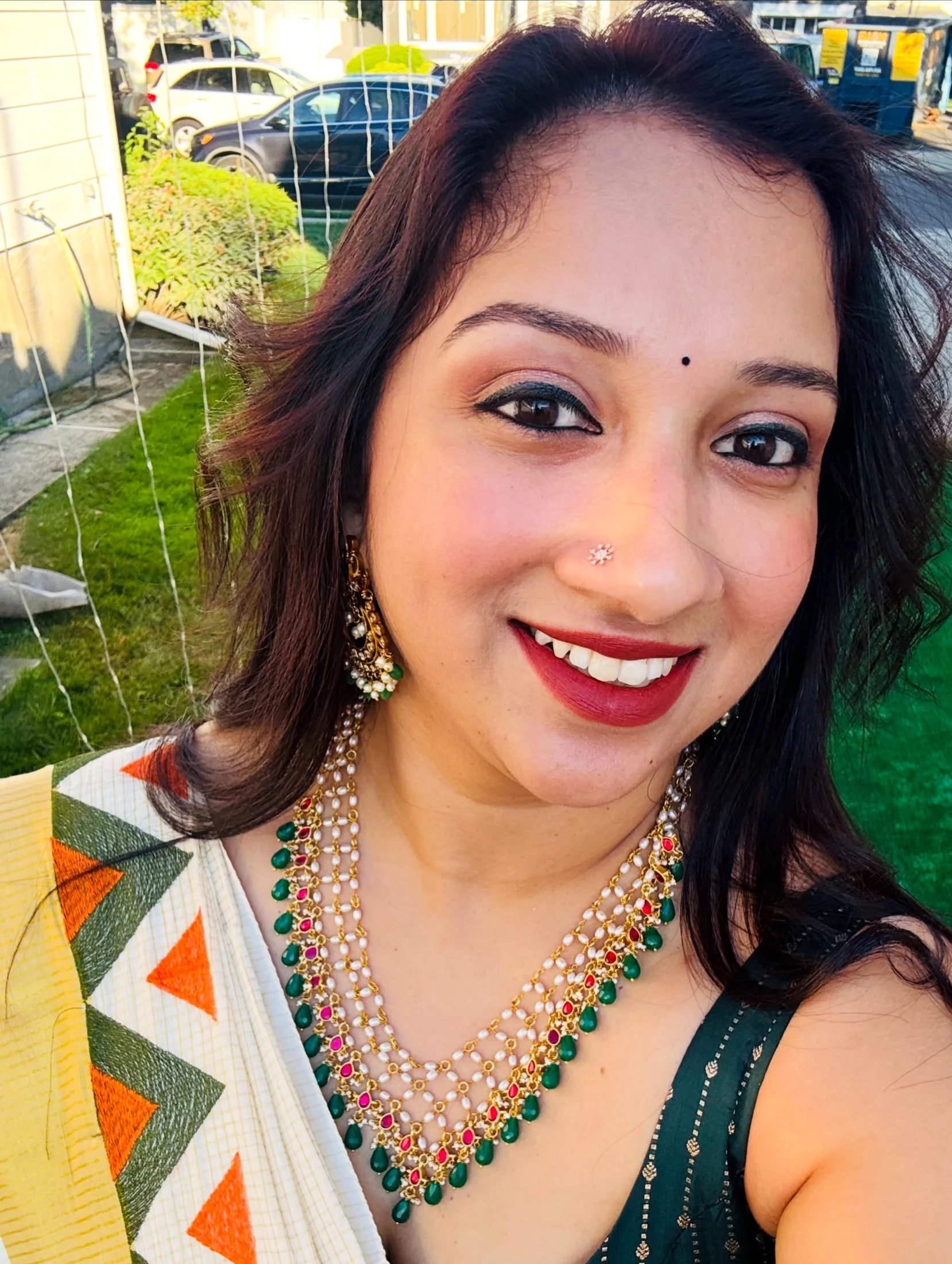 Close view of a layered pearl necklace set with red and green stones worn by an Alankara model